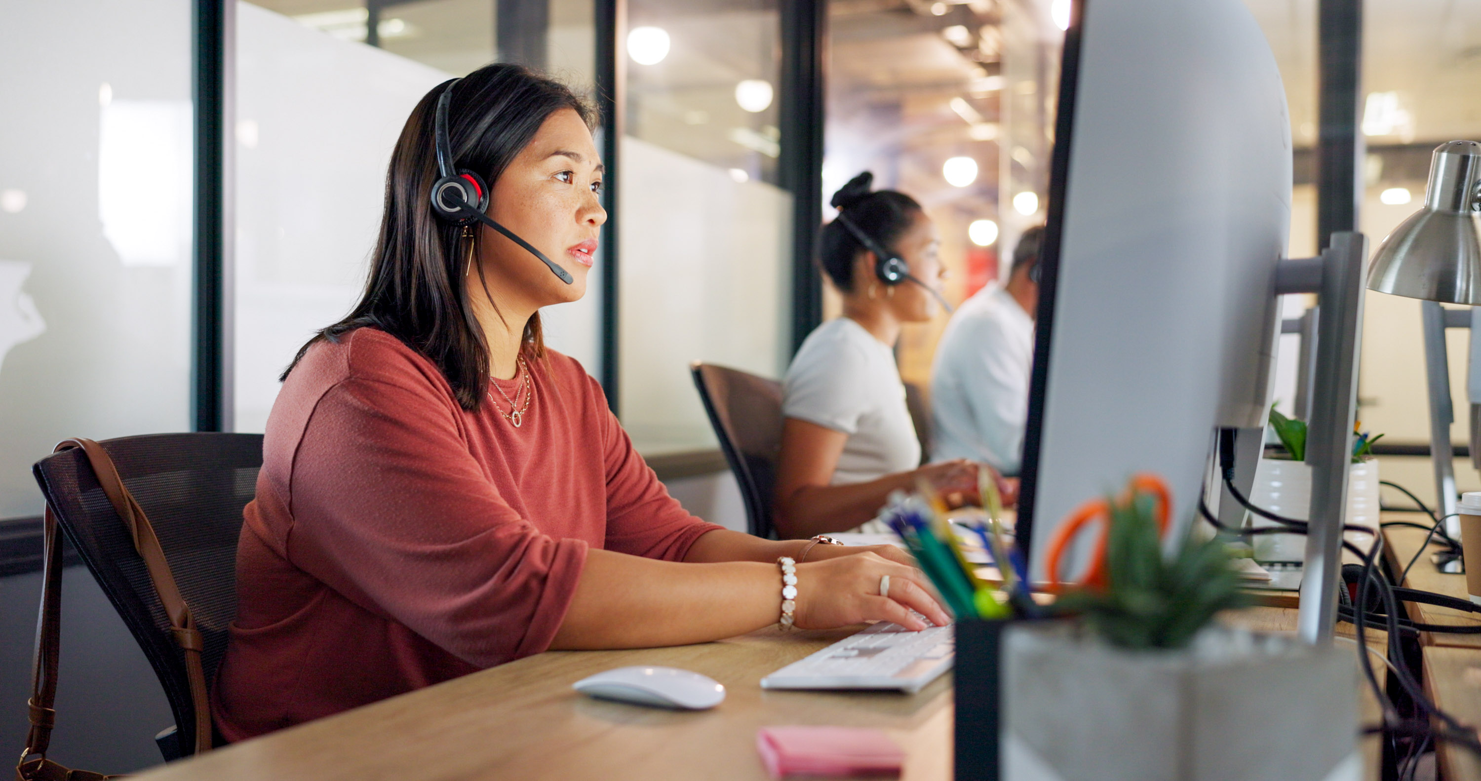 Woman with a headset attentively working at a computer in a modern office environment.